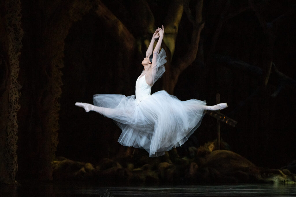 Danbi Kim soars in a saut de chat, arms in high fifth, onstage as Myrtha. She wears a long, white Romantic tutu with arm puffs.