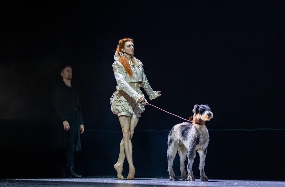 Harvey Littlefield, dressed as Mary, Queen of Scots, walks a prop dog onstage.