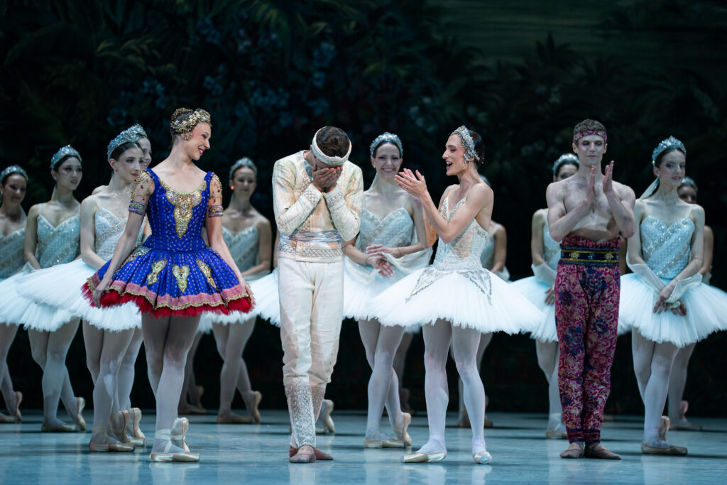 Onstage during curtain call, Thomas Docquir places his head in his hands as he is overwhelmed with happy emotion. Dancers around him in costume clap and celebrate.