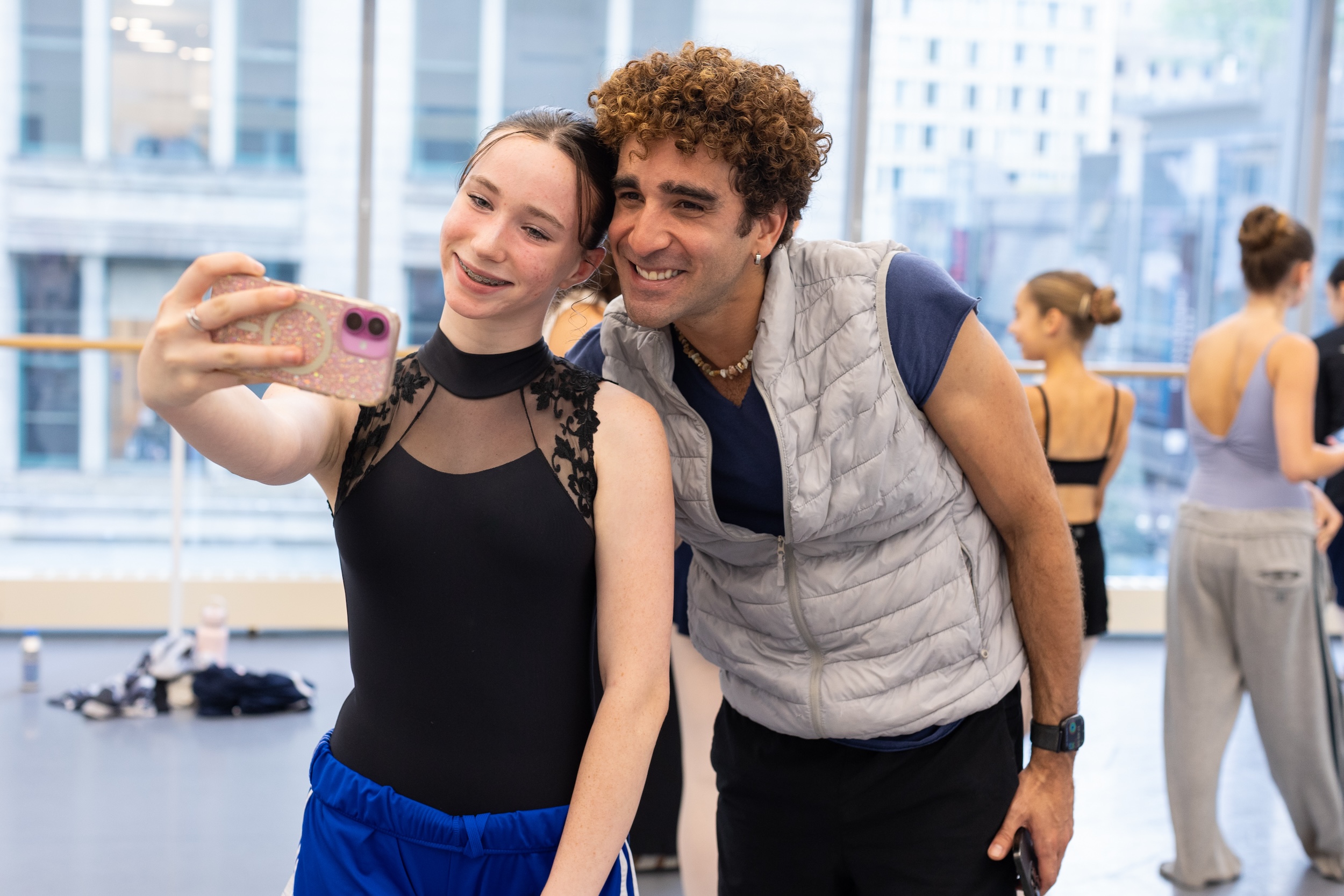 A teenage ballet student holds her phone in front of her to snap a selfie with her ballet teacher.