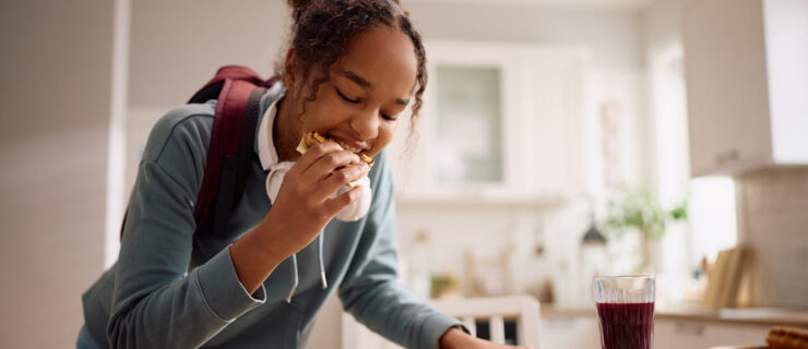 A teenage girl eating breakfast in a hurry before leaving for school.