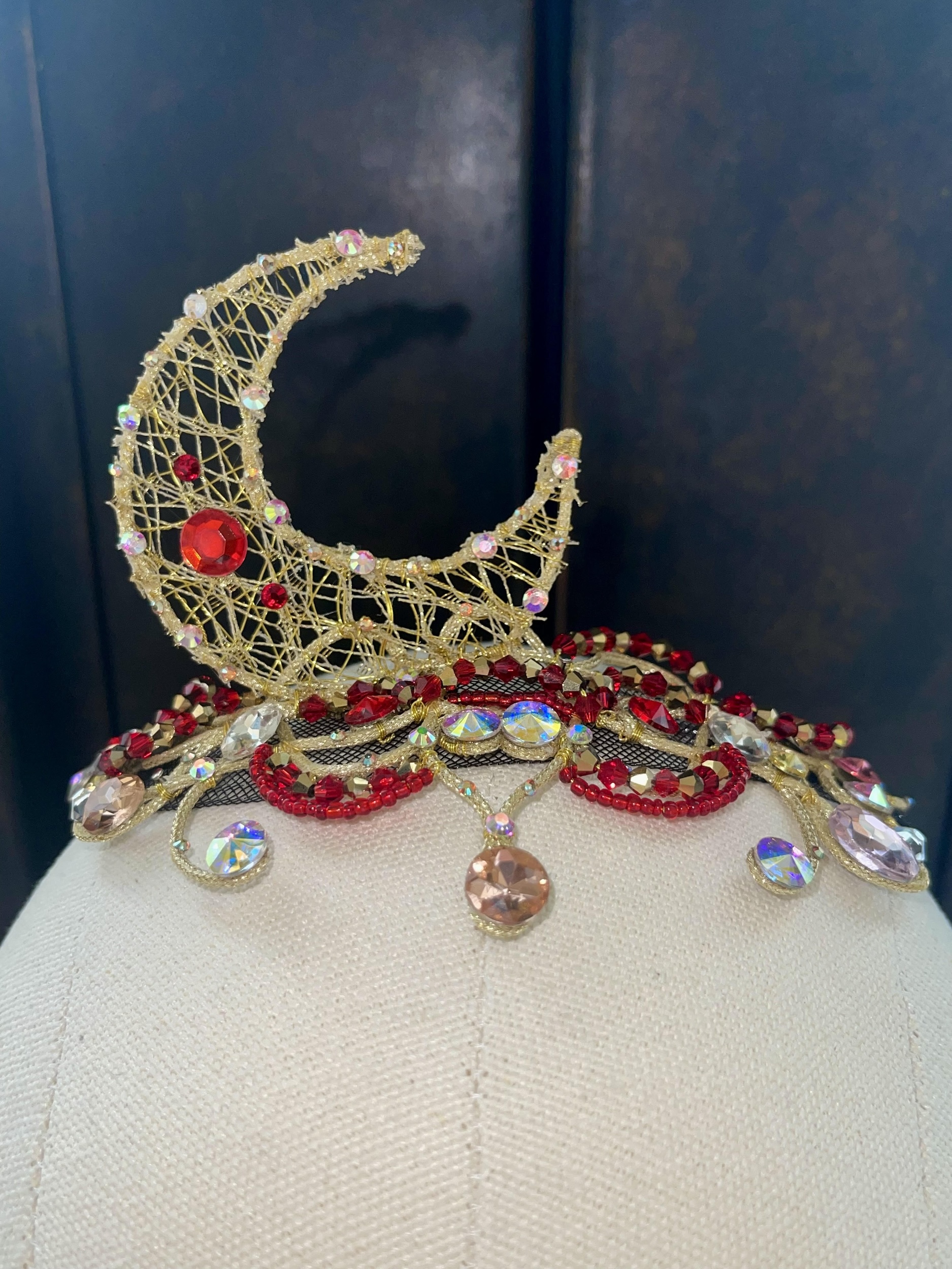 A ballet costume tiara that features a golden crescent moon with red, pink and silver gems.