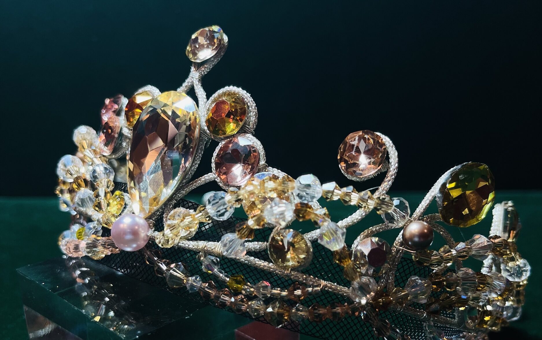 A close-up of a ballet costume tiara with white, amber, and light pink gems.