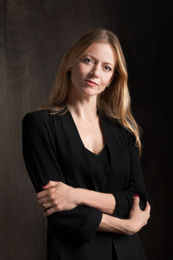 Julia Erickson, wearing black formal attire, folds her arms across her body and peers into the camera serenely for her headshot.
